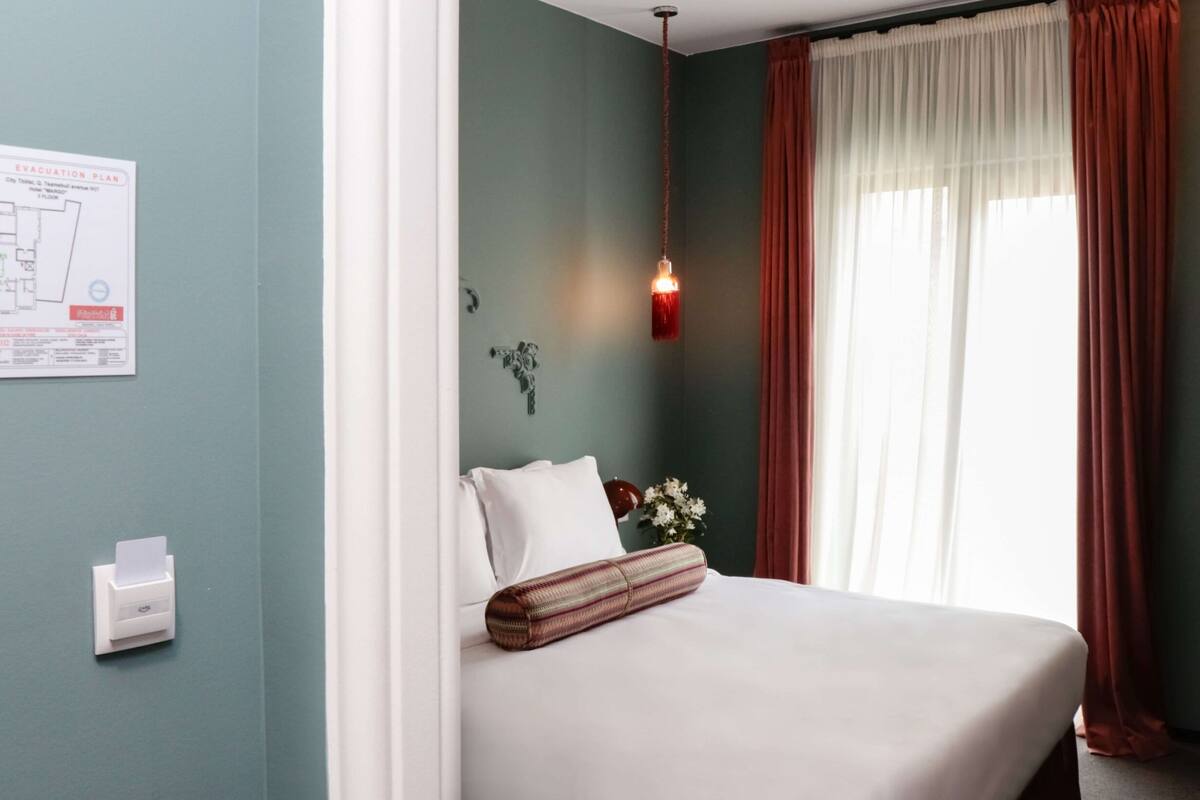 A hotel room with a bed, a wall-mounted emergency exit plan, a wall-mounted paper dispenser, and a hanging pendant light.