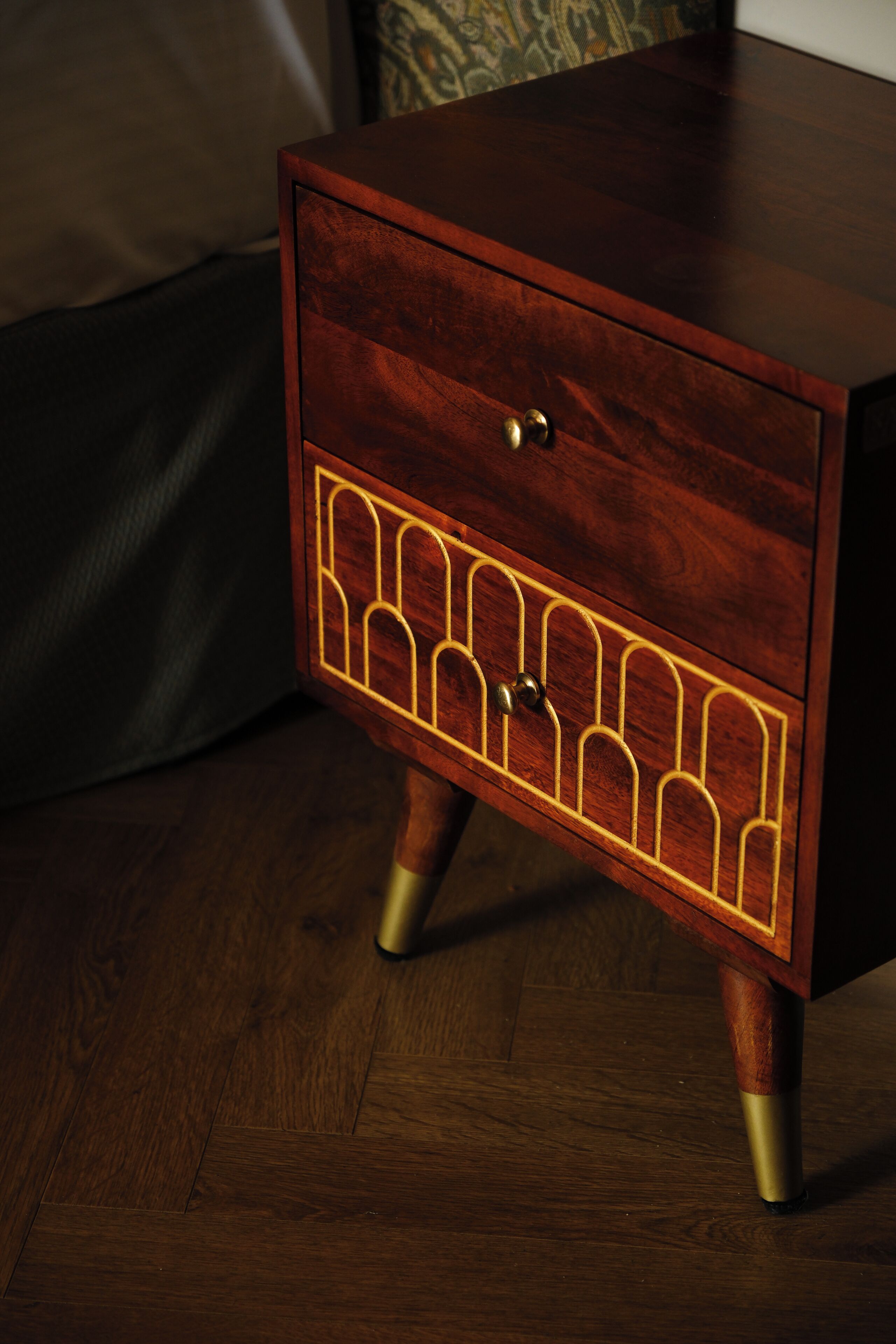 A wooden nightstand with a drawer, a decorative panel, and a brass handle.