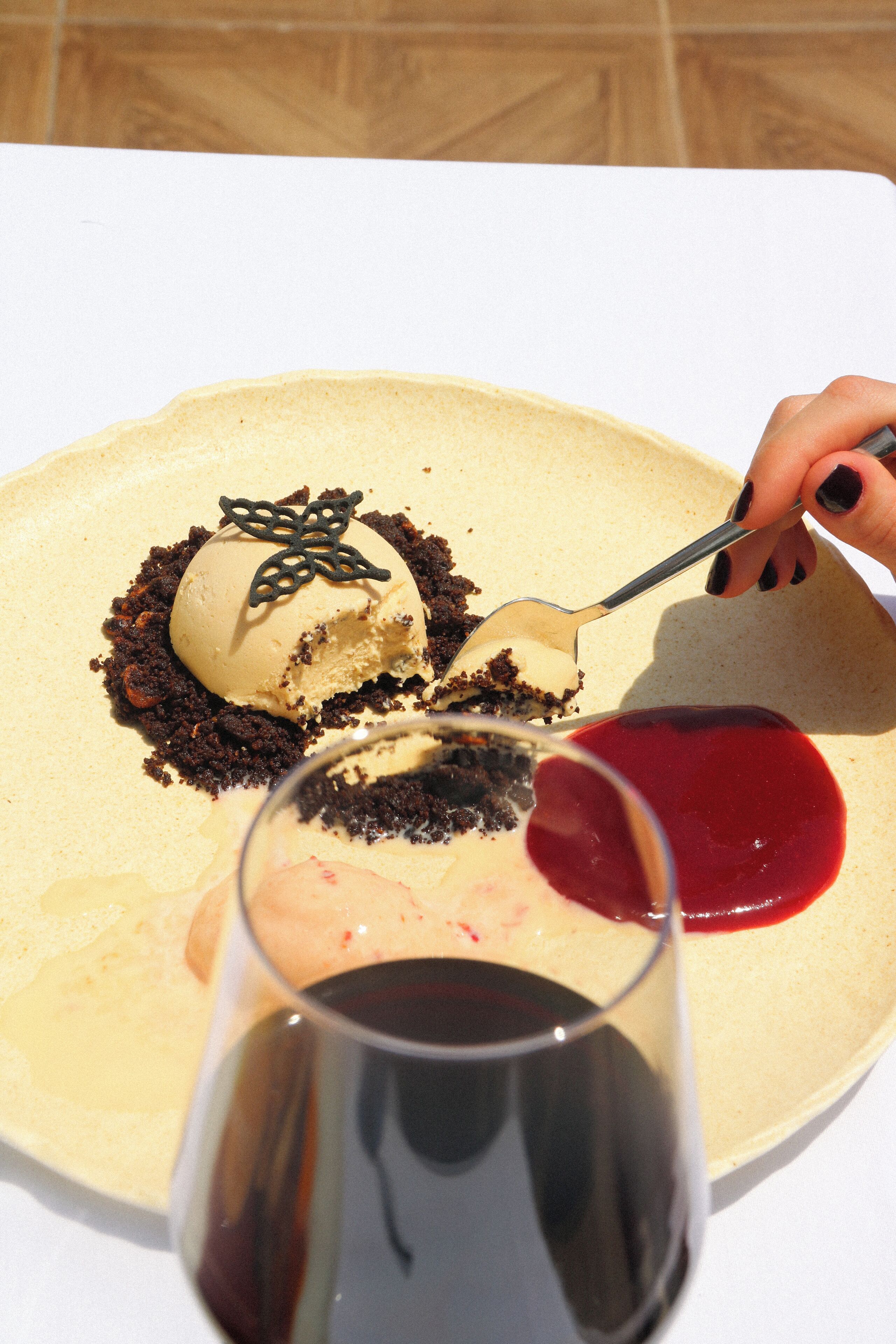 Un plato de postre con una bola de helado, un trozo de pastel y una copa de vino tinto.