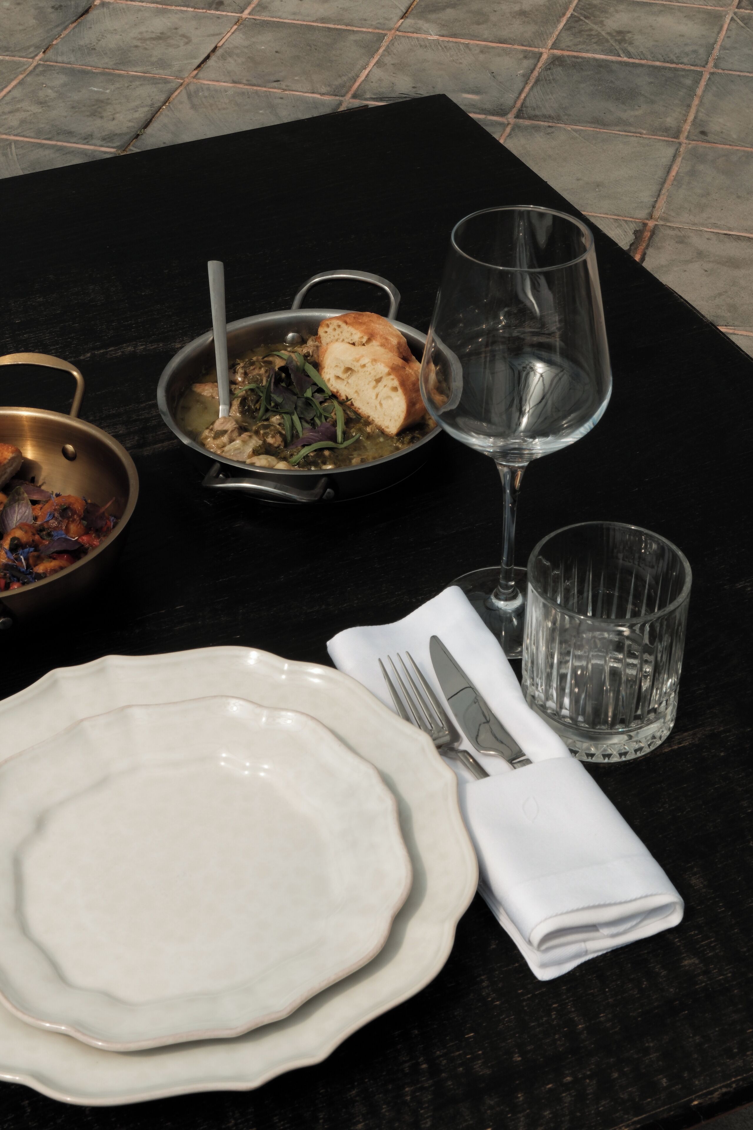 A dining table with a plate, cutlery, a glass, and a bowl of food.