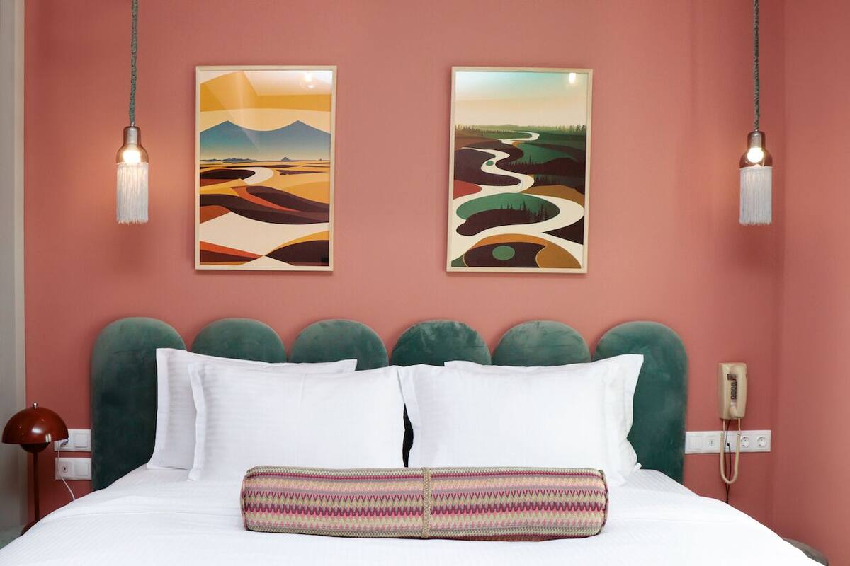 A bed with white linens, a green upholstered headboard, and two wall-mounted paintings depicting abstract landscapes.