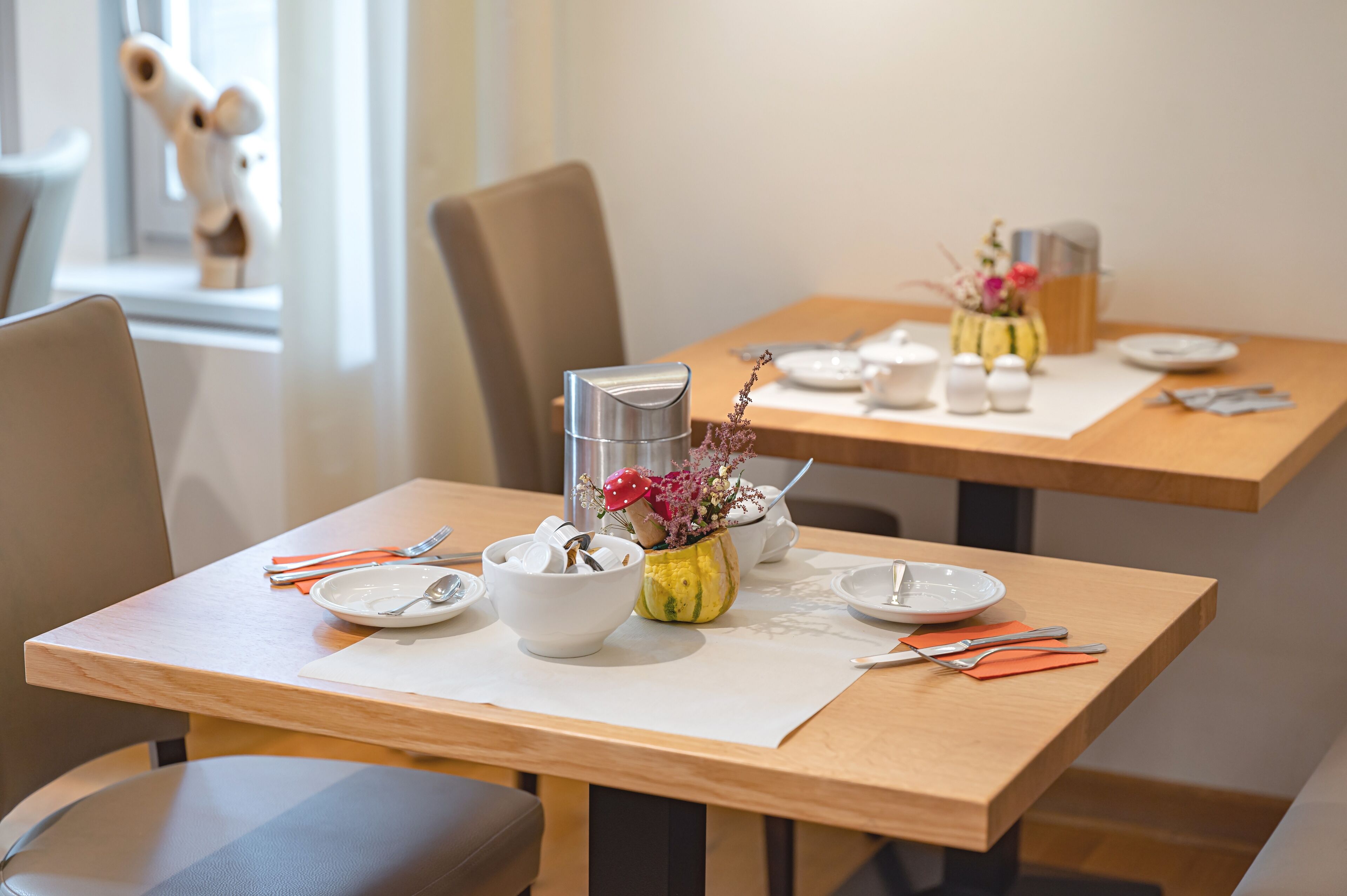 A dining area with wooden tables, white plates, bowls, and cutlery.