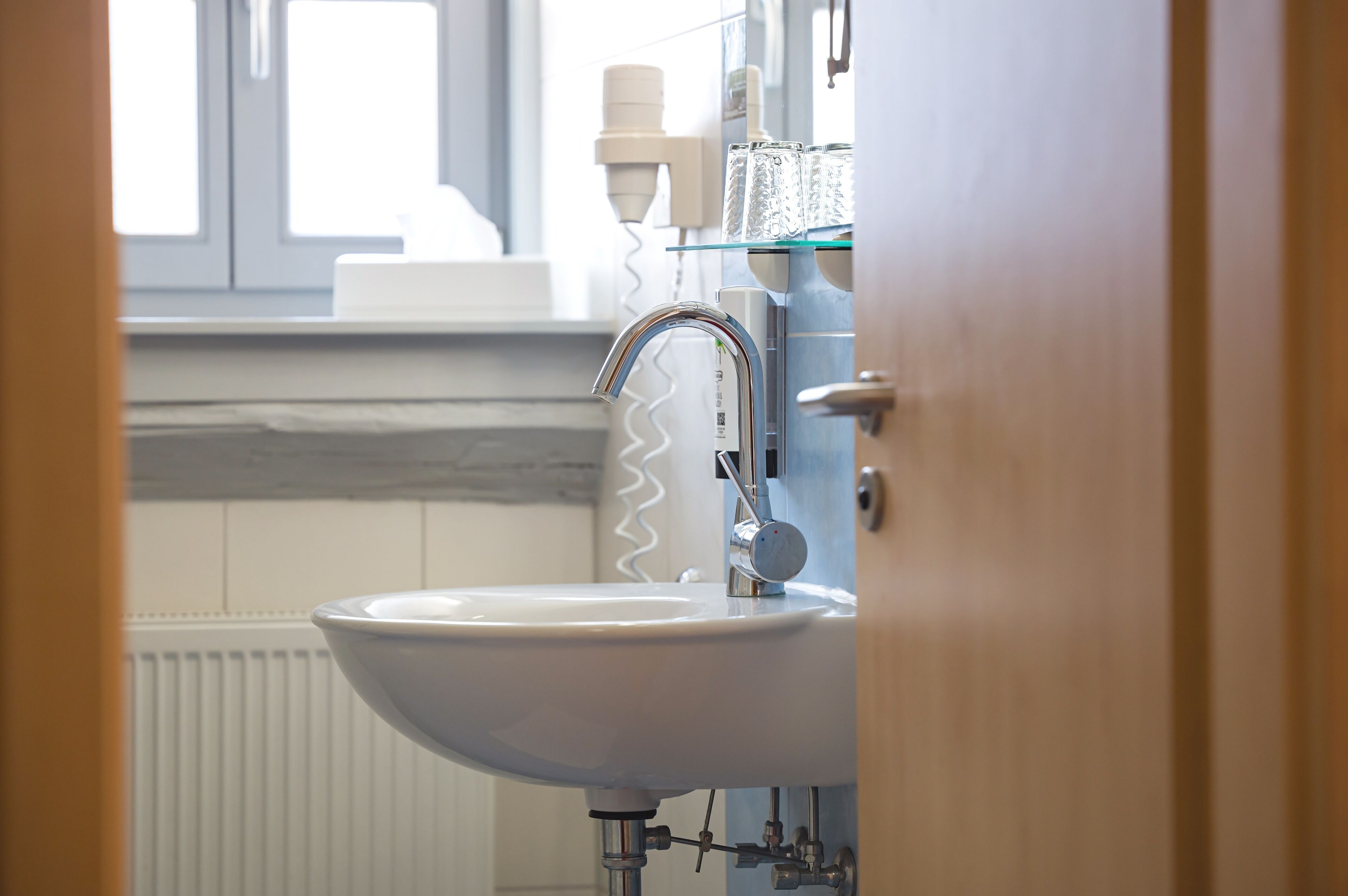 A bathroom with a white sink, chrome faucet, and a glass shelf with toiletries.