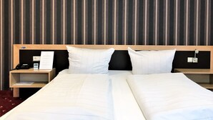 A hotel room with a double bed, two bedside tables, a nightstand, and a striped wall. - Hotel Mühlhäuser Hof (Mühlhausen/Thüringen)
