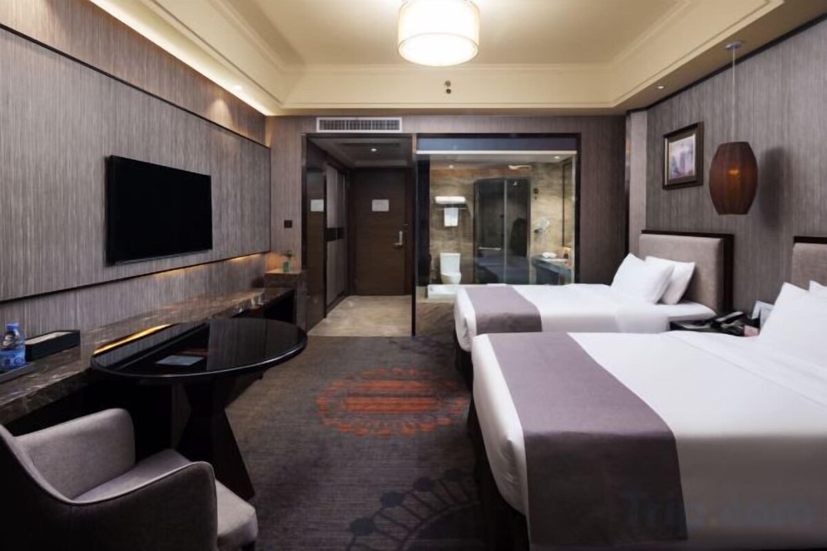 Habitación de hotel con dos camas, televisión, escritorio y zona de estar.