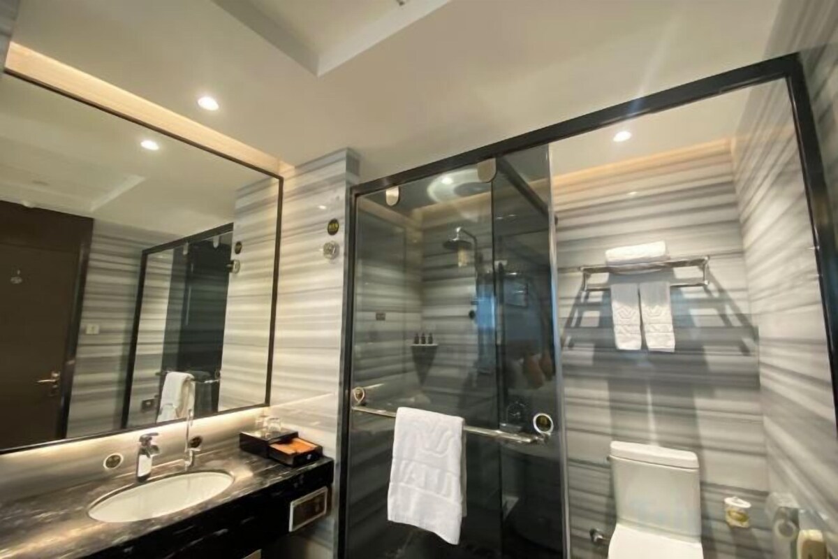 A modern bathroom with a glass-enclosed shower, a marble-tiled wall, and a large mirror.