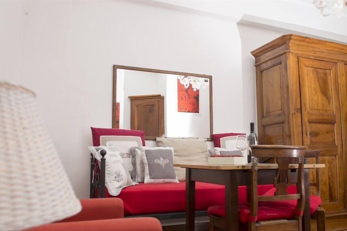 Une pièce chaleureuse avec un meuble en bois, un canapé rouge et une petite table sur laquelle se trouvent une bouteille et un livre.