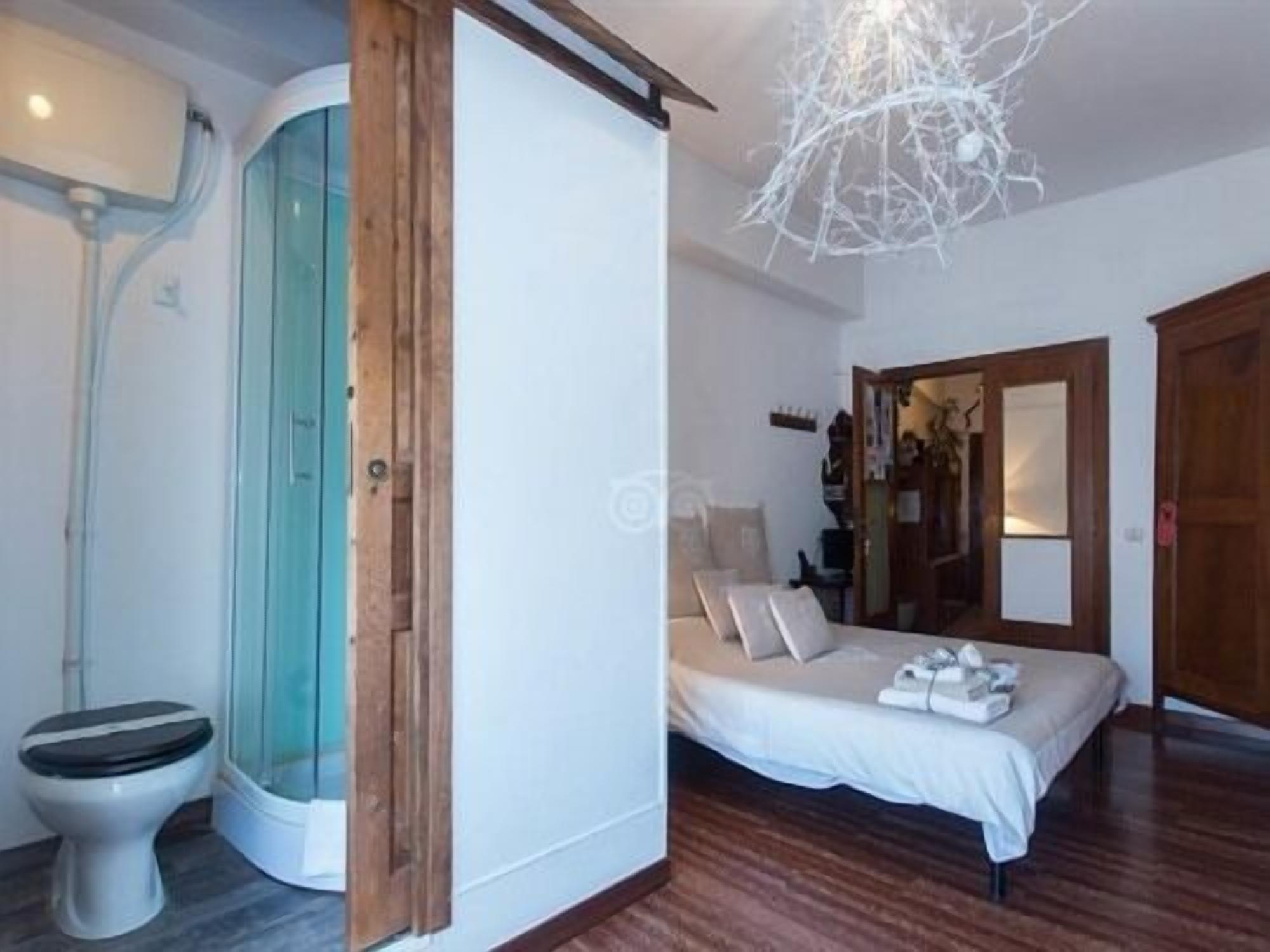 Une chambre à coucher avec un lit, un plancher en bois, un mur blanc et une salle de bain équipée de toilettes et d’une douche.