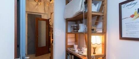 A narrow hallway with a wooden ladder shelf filled with kitchenware and a framed picture on the wall.