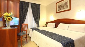 A hotel room with a wooden headboard, a large bed with white bedding, a desk with a television, and a vase with flowers. - AdoraSuite B&B (Rome)