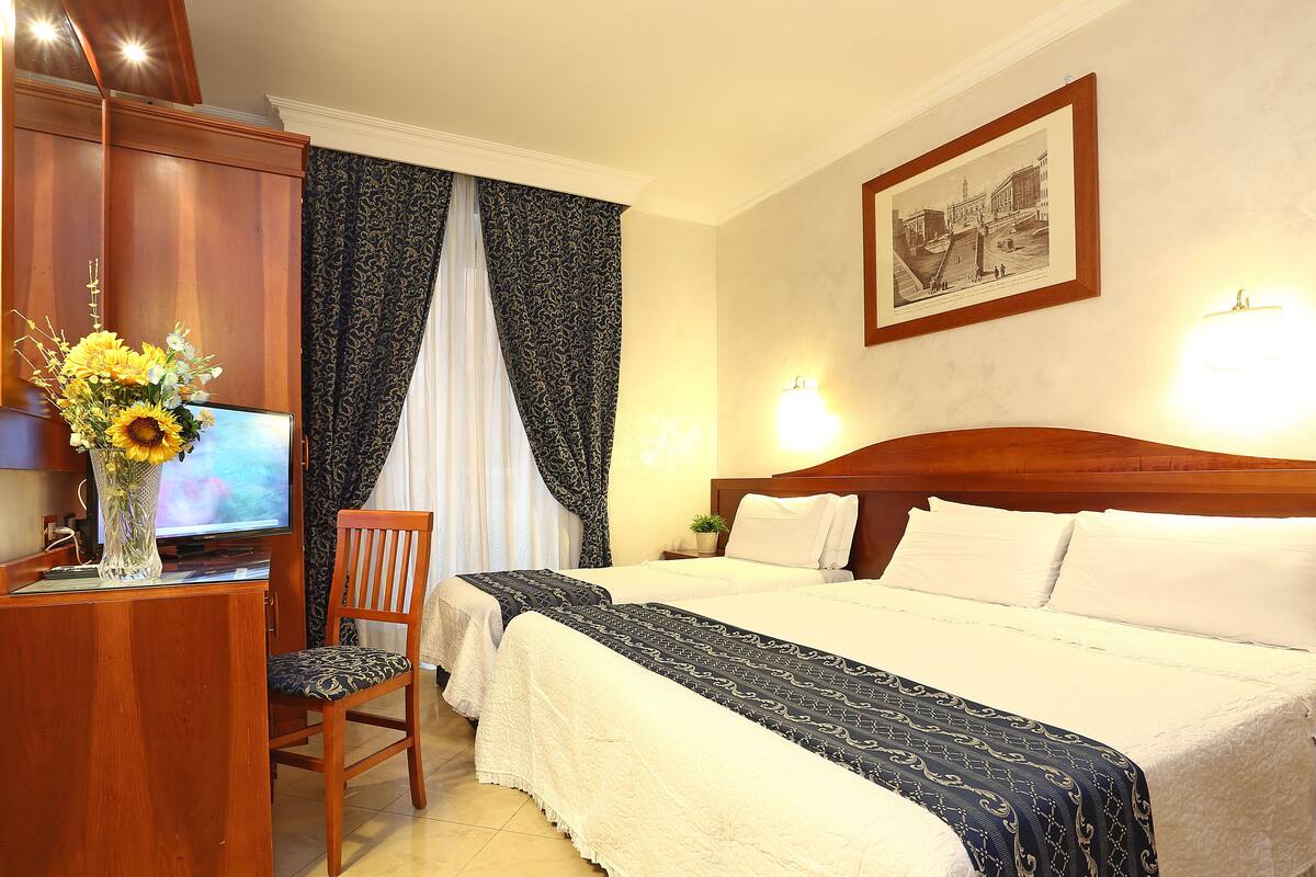 A hotel room with a wooden headboard, a large bed with white bedding, a desk with a television, and a vase with flowers.