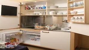 A compact kitchen with a built-in refrigerator, a sink, and shelves for storage. - AdoraSuite B&B (Rome)
