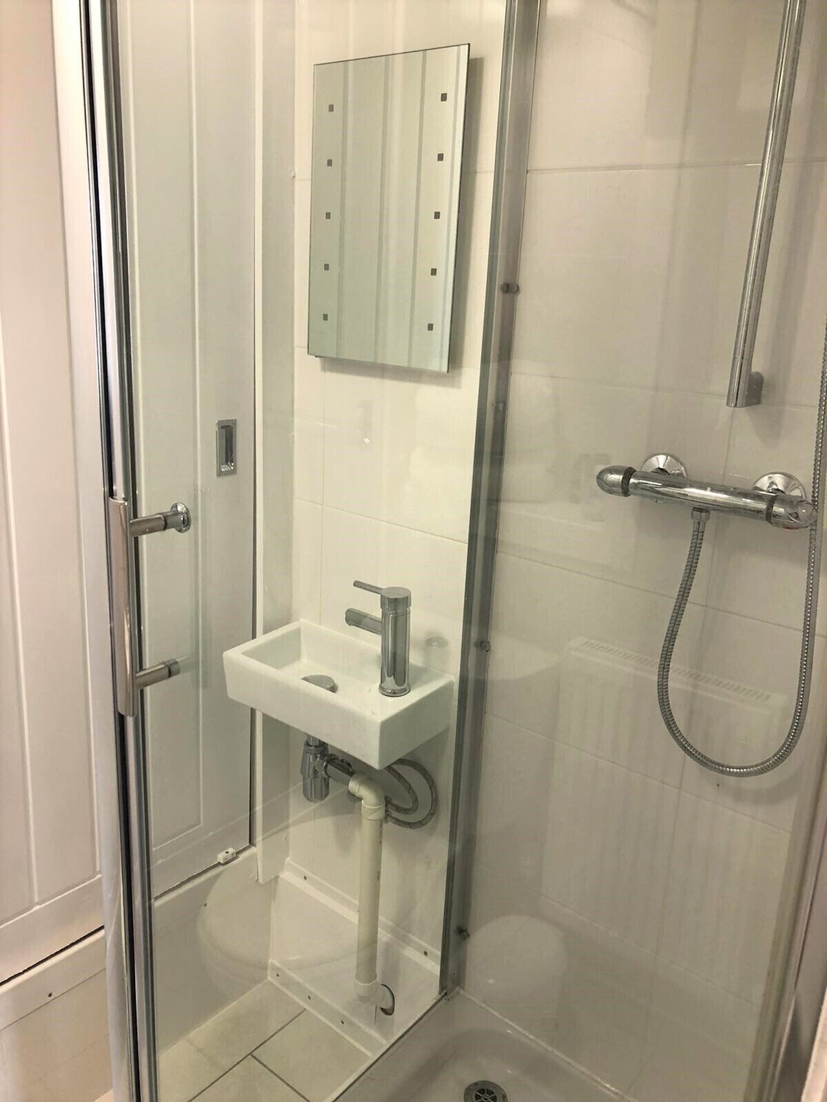 A glass-enclosed shower with a white sink and a mirror above it.