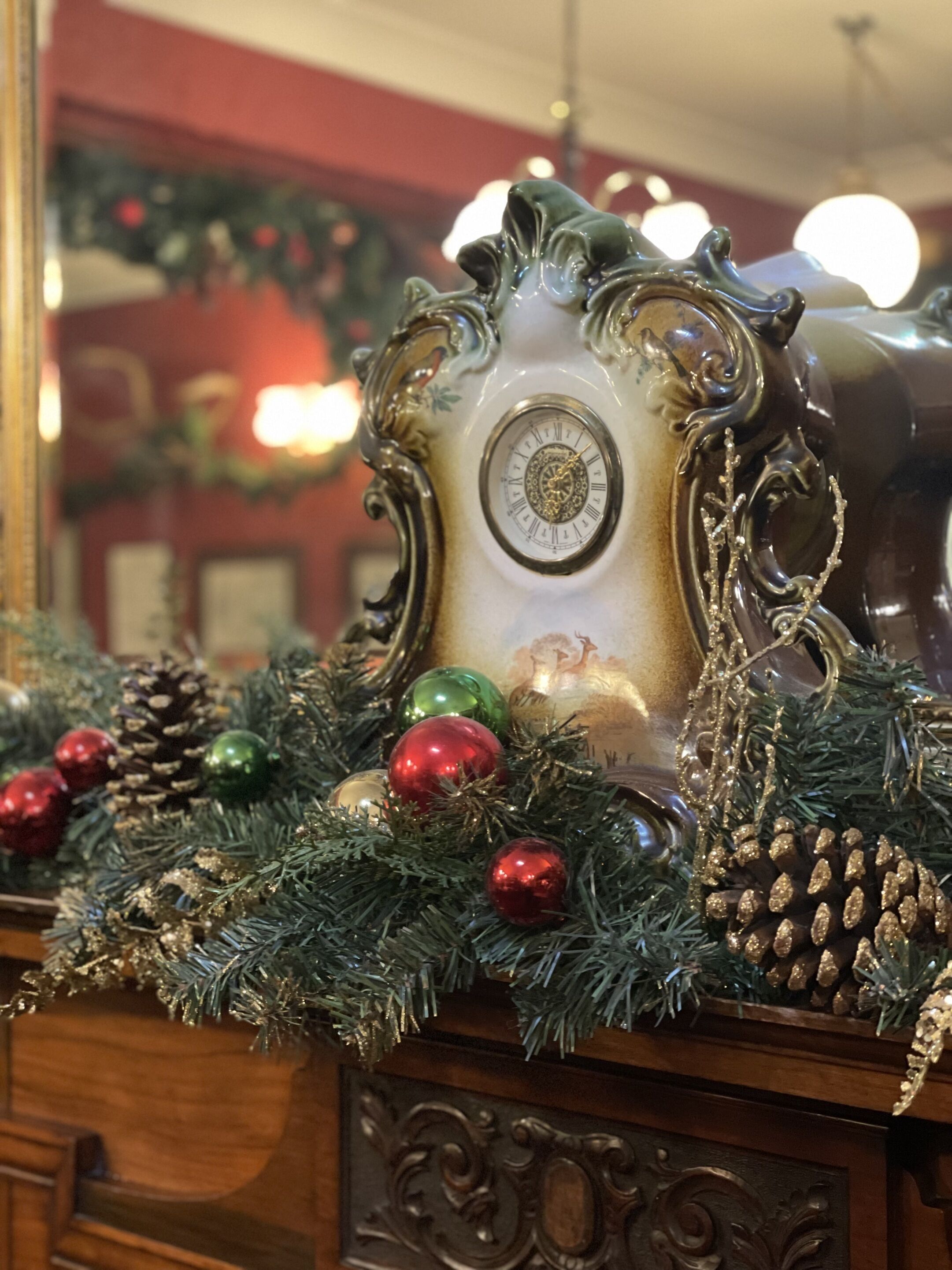 A clock with ornate carvings and a decorative garland with pine cones and ornaments.
