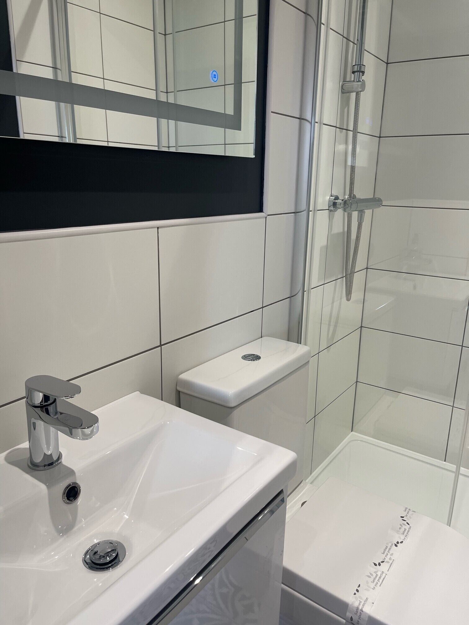 A modern bathroom with a white sink, mirror, and shower.