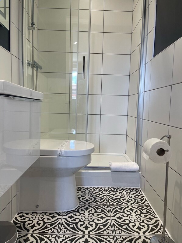 A modern bathroom with a toilet, shower, and patterned floor tiles. - The Horseshoe and Castle (Rochester)