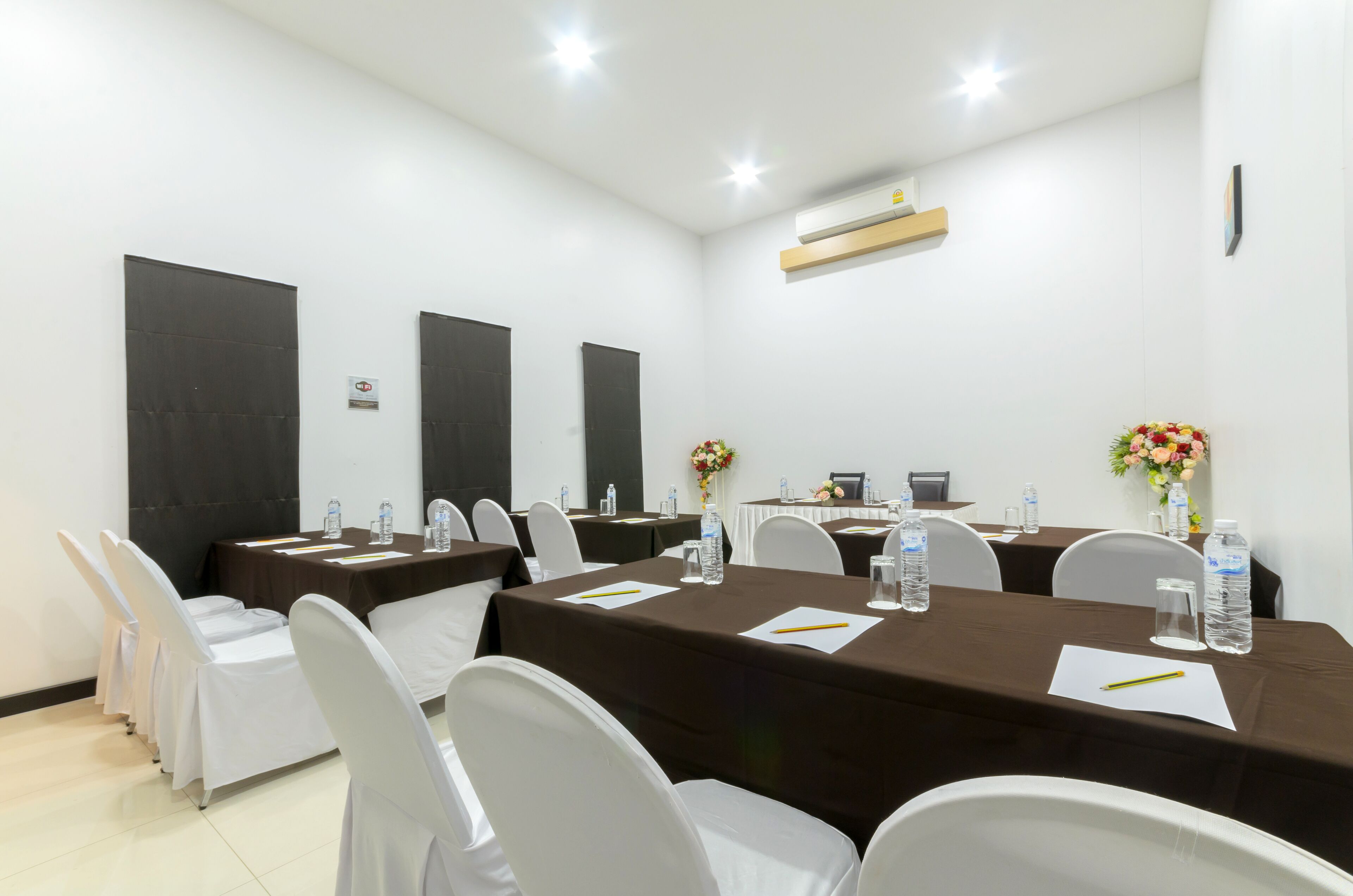 A conference room with multiple tables, white chairs, water bottles, and floral centerpieces.
