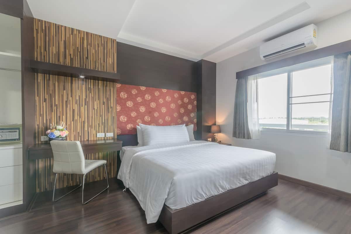 Een moderne hotelkamer met een groot bed, een bureau en een stoel. Er is een raam met gordijnen en een airconditioner aan de muur.