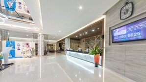 Un moderno vestíbulo de hotel con un mostrador de recepción, un reloj y una pantalla digital mostrando un número de teléfono.