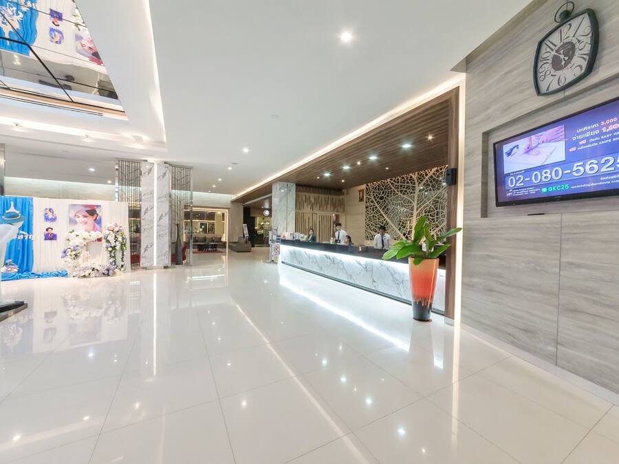Un hall d’hôtel moderne avec un comptoir d’accueil, une horloge et un écran numérique affichant un numéro de téléphone.