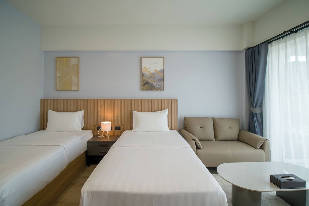 Een hotelkamer met twee eenpersoonsbedden, een slaapbank, een kleine tafel en een nachtkastje met lamp.