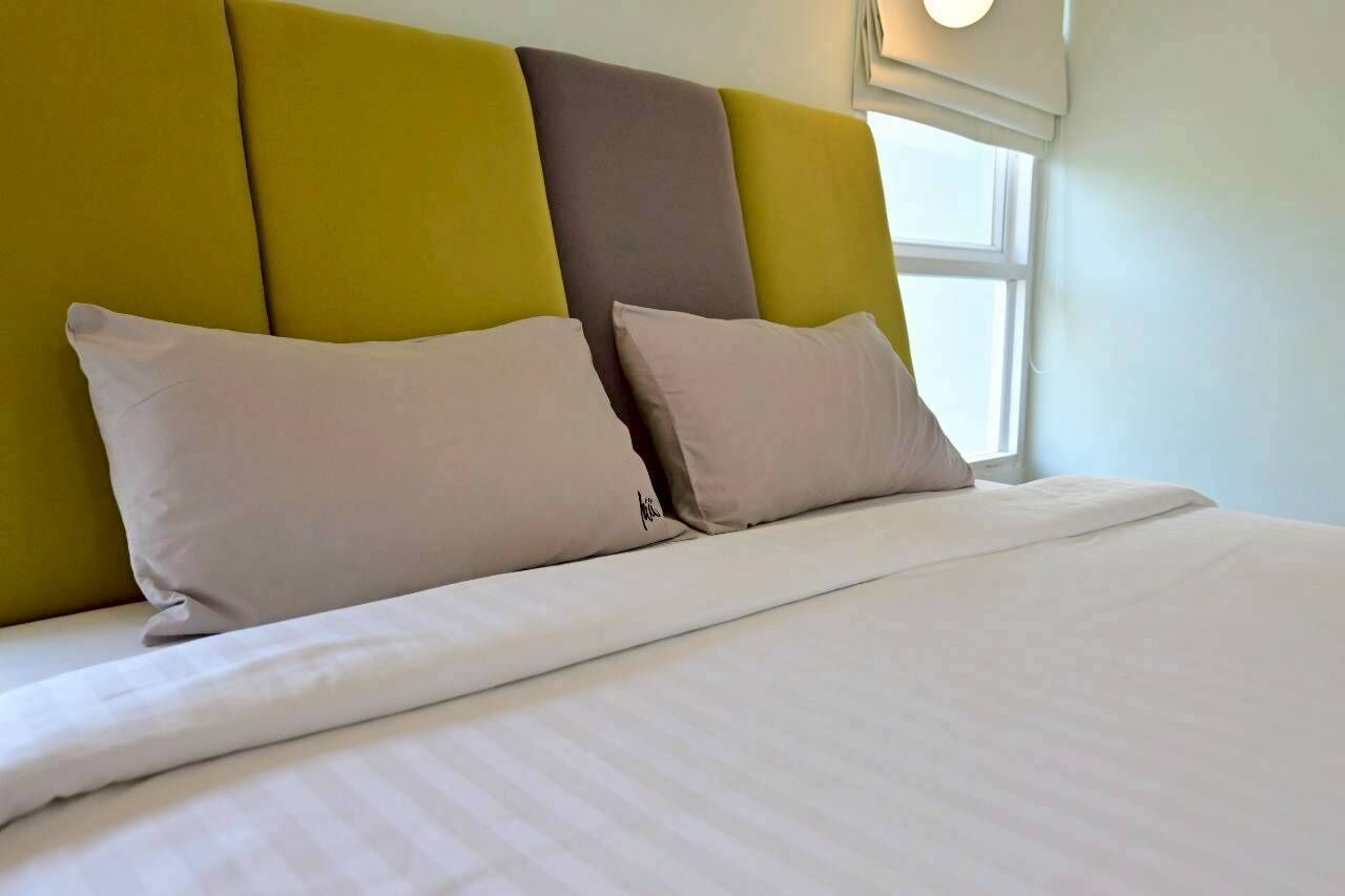 Una cama con cabecera en amarillo y gris, dos almohadas y una ventana con luz diurna.
