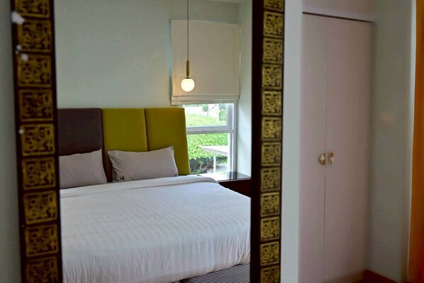 A bedroom with a bed, a window with a view, a door, and a hanging light fixture.