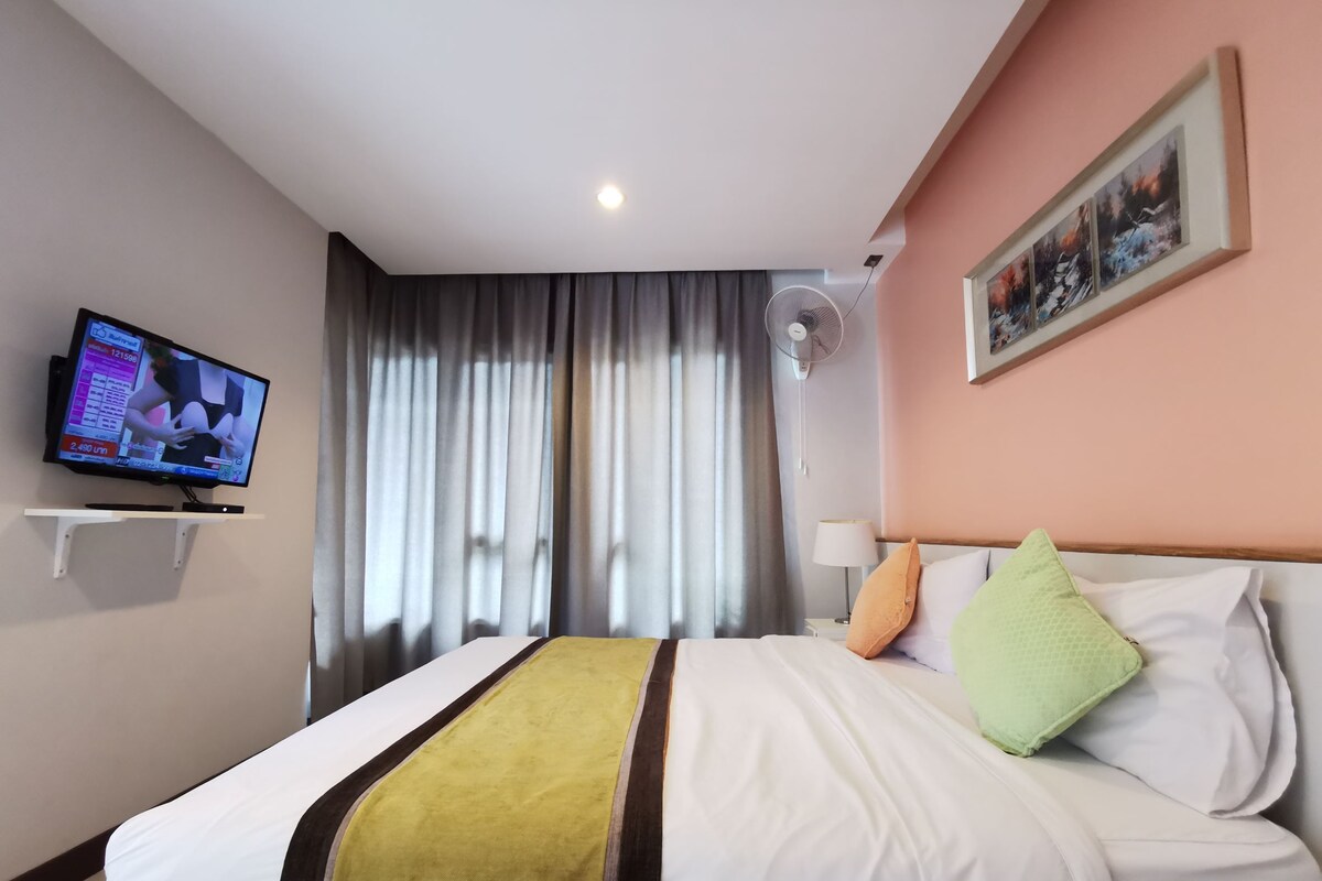 Quarto de hotel com cama, televisão em suporte, ventoinha na parede e um quadro.