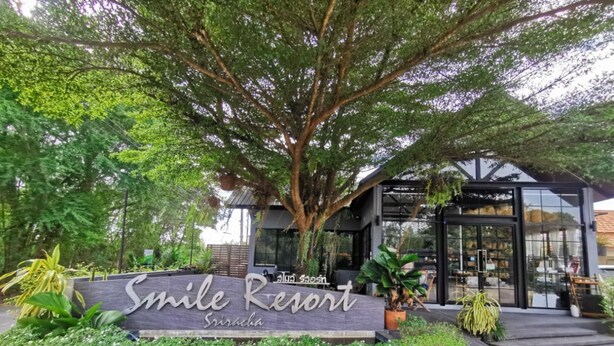 A sign for Smile Resort in Srishala, surrounded by lush greenery and a modern building structure. - Smile Resort Sriracha (Si Racha)