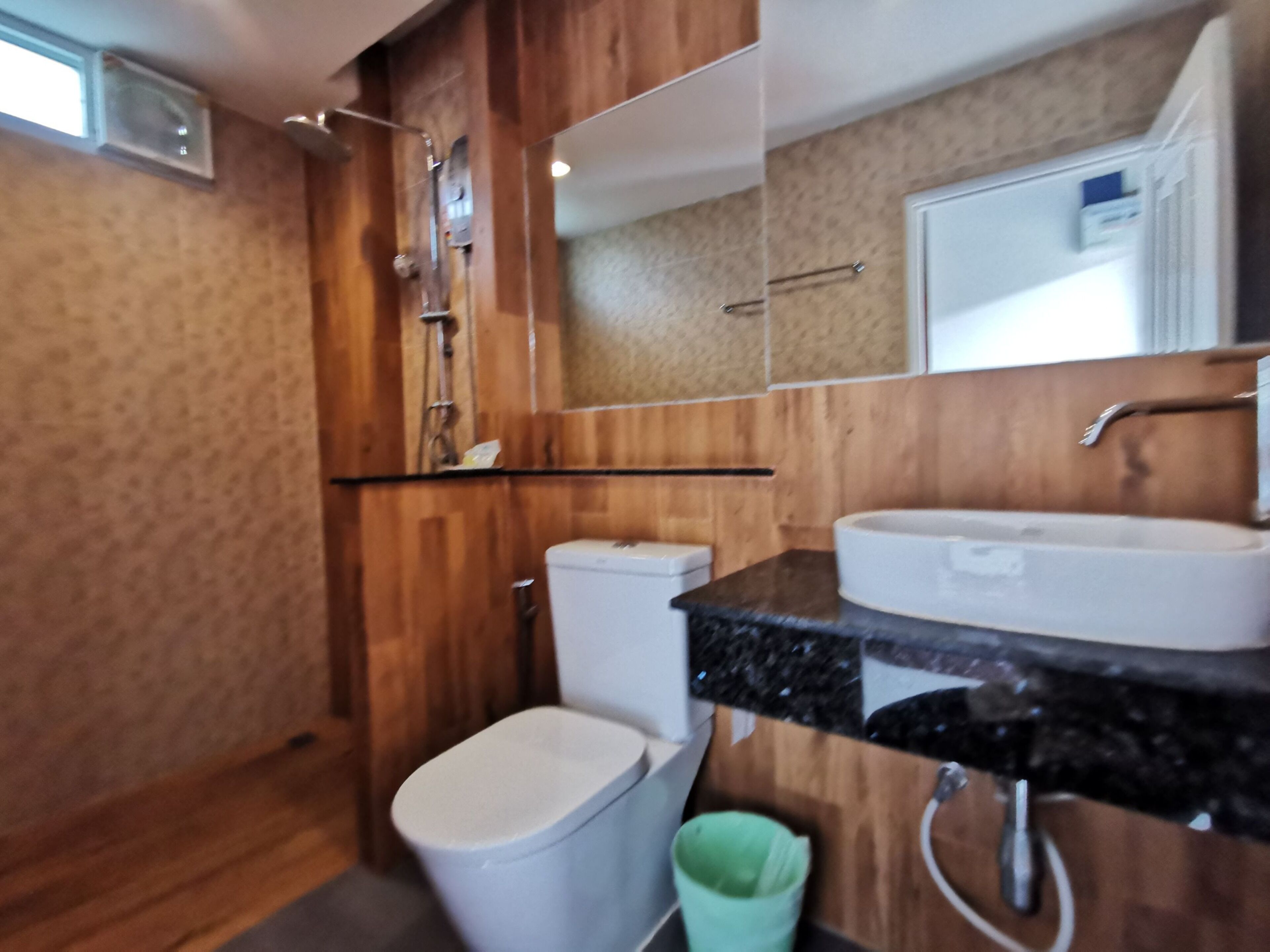 A bathroom with a wooden wall, a white toilet, a sink with a mirror, and a shower area.
