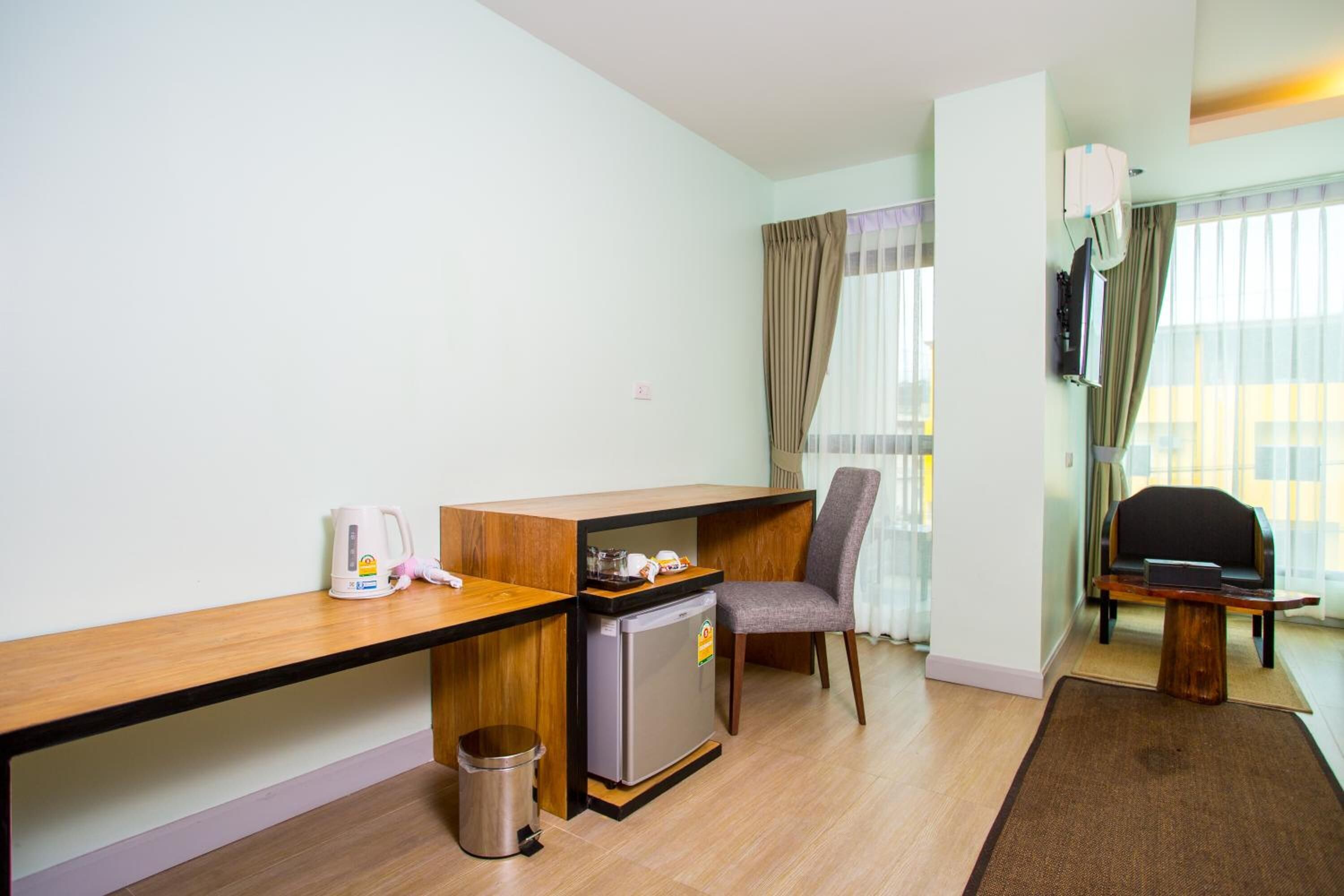 A compact hotel room with a kitchenette, a single chair, a small table, and a TV mounted on the wall.