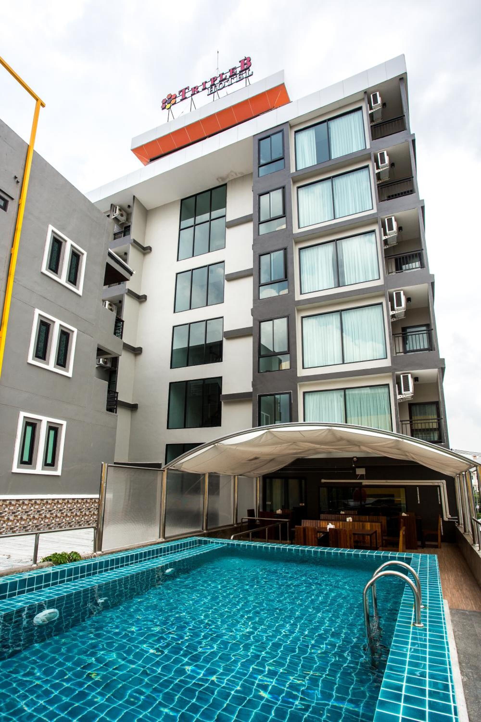A modern hotel with a swimming pool, multiple balconies, and a covered outdoor seating area.