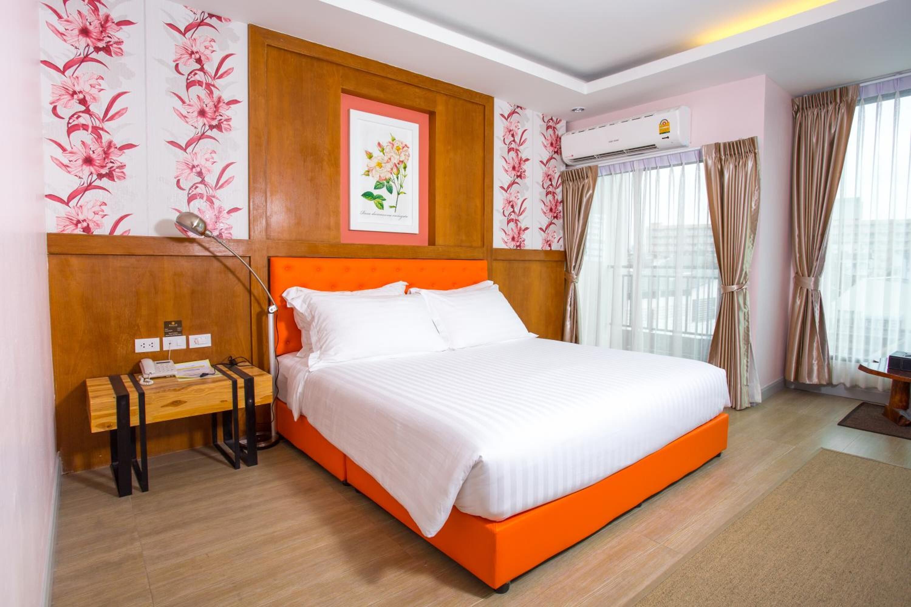 A hotel room with a large bed, a wooden nightstand, a desk, and a wall-mounted air conditioner.