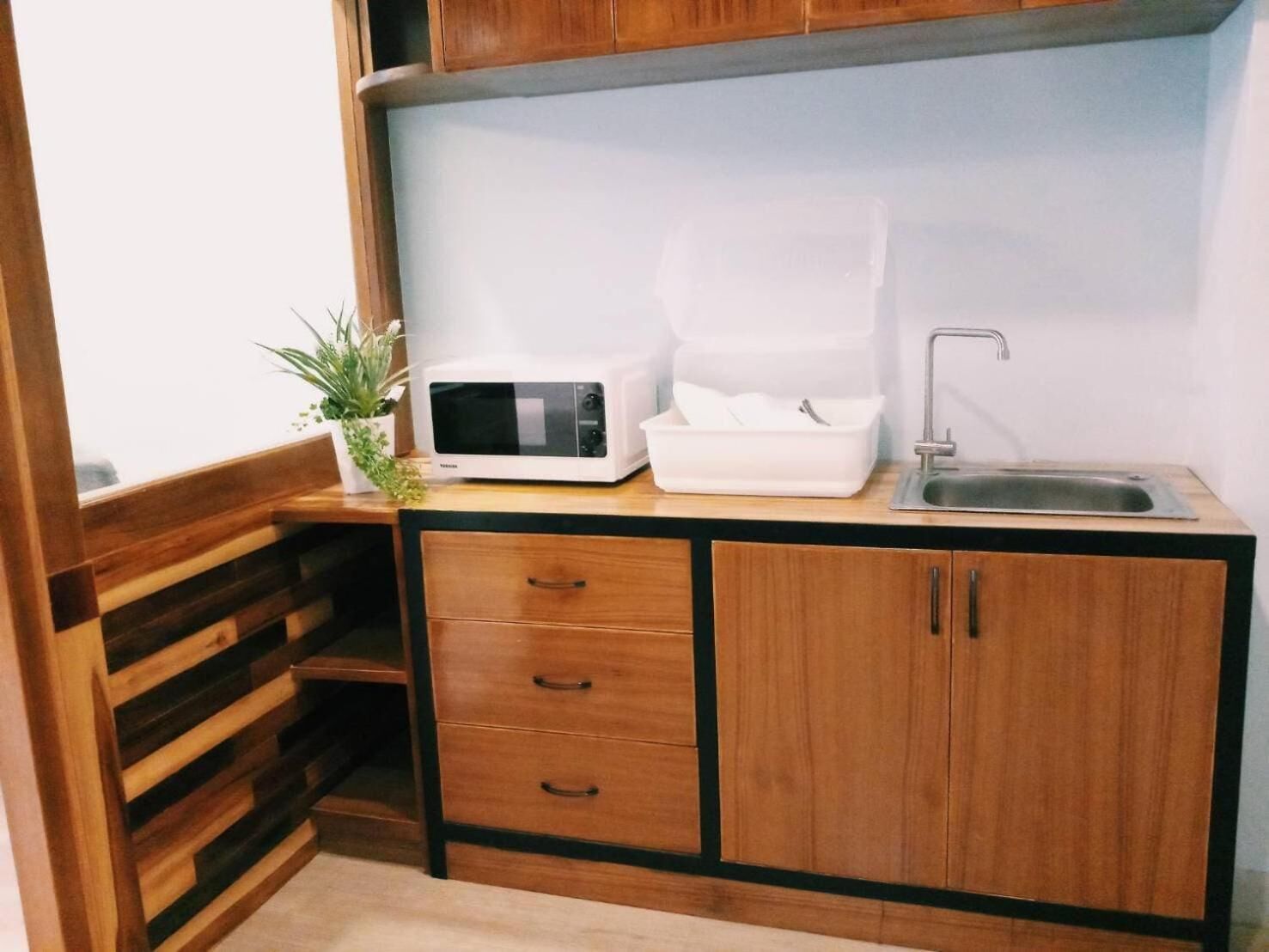 A compact kitchenette with a microwave, a sink, and wooden cabinets.