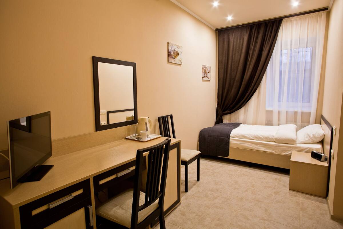 A compact hotel room with a bed, a desk with a chair, a television, and a window with curtains.