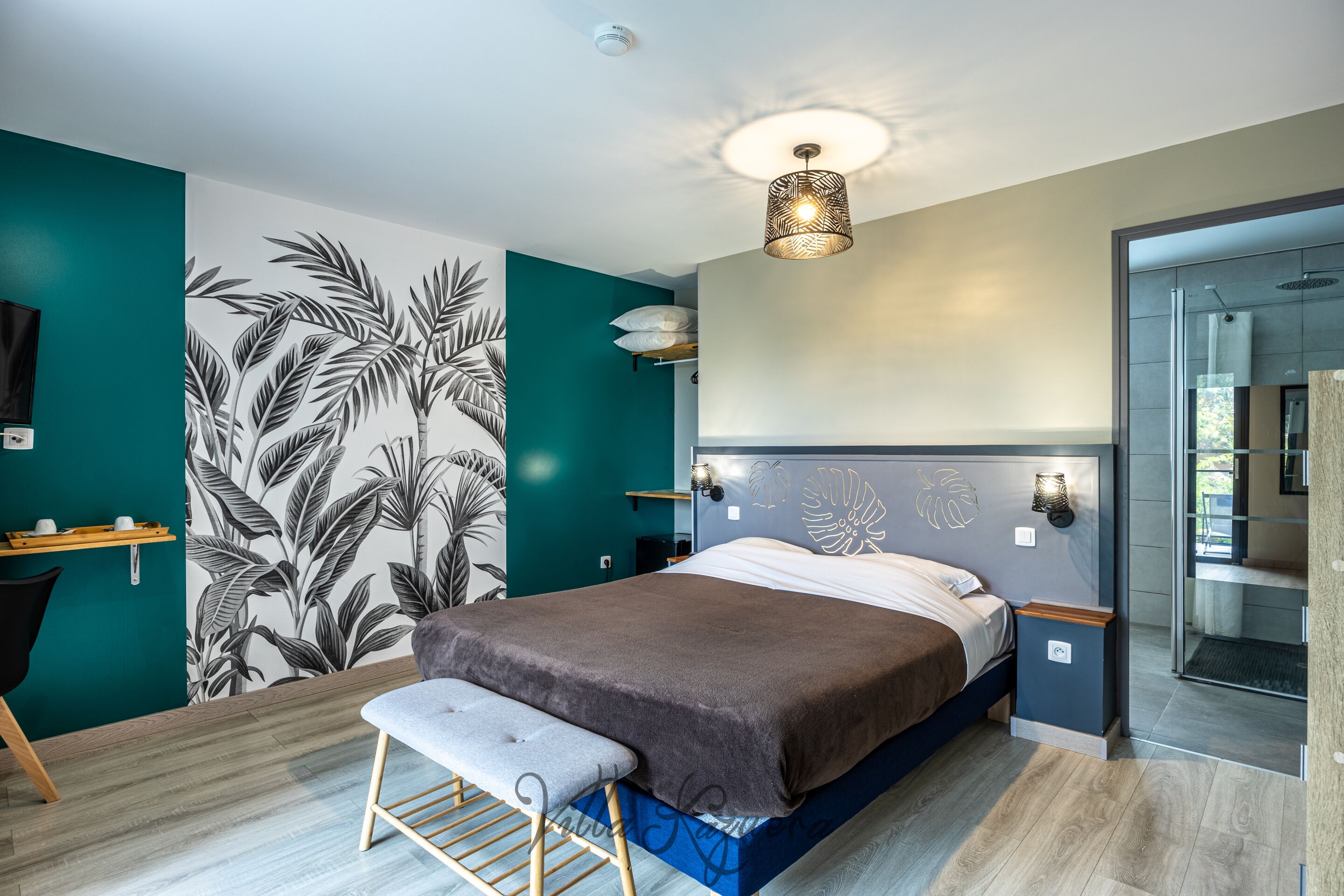 Une chambre moderne avec un lit, un banc, des œuvres d’art mural et un luminaire au plafond.