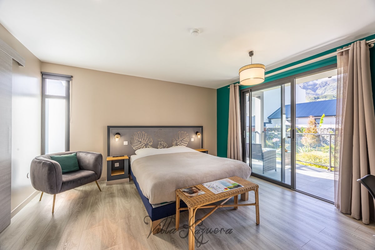 Une chambre d’hôtel moderne dotée d’un grand lit, d’un canapé, d’une petite table et d’un balcon offrant une vue sur les montagnes.