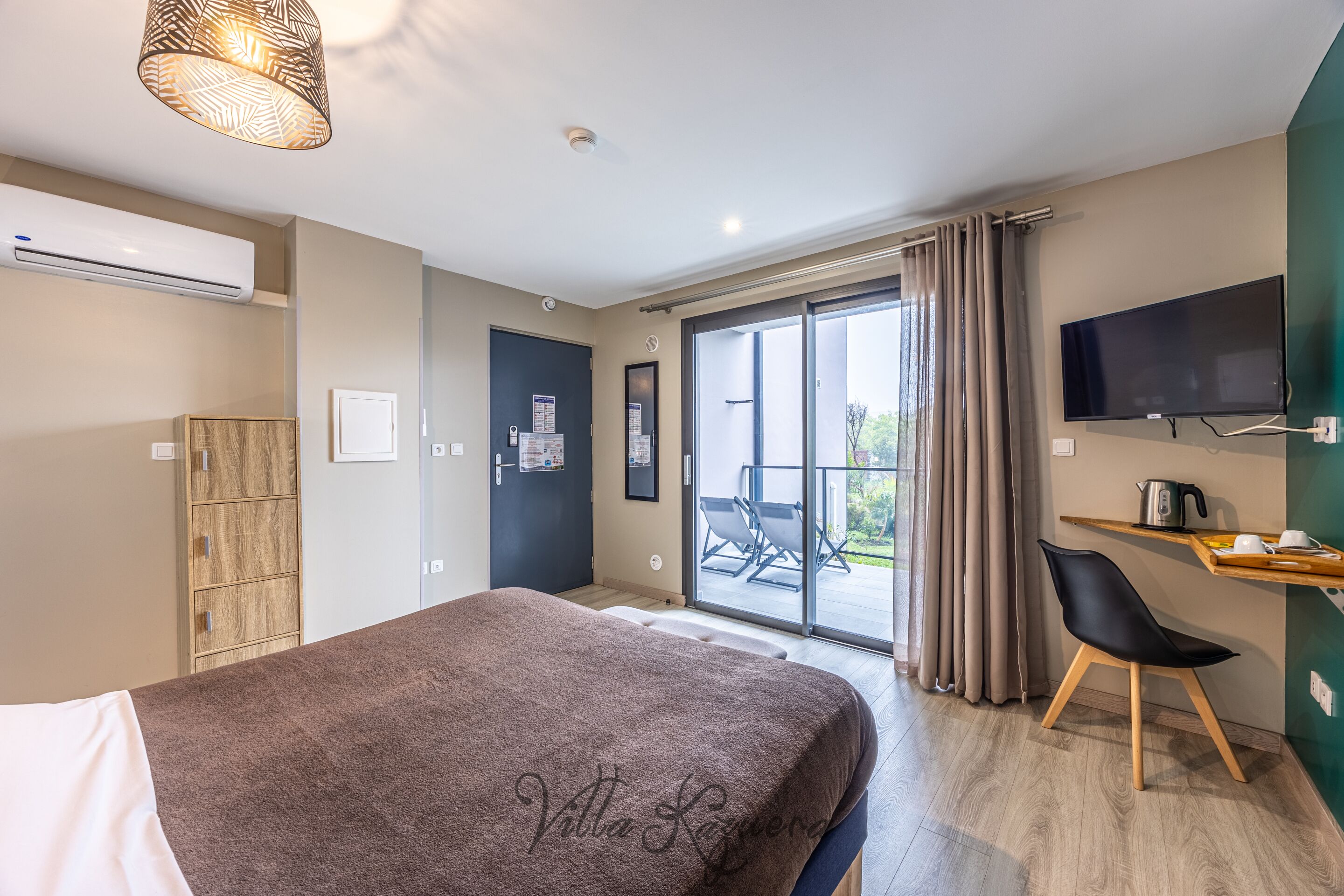 A modern hotel room with a large bed, a TV mounted on the wall, a sliding glass door to the balcony, and a wooden cabinet.
