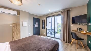 A modern hotel room with a large bed, a TV mounted on the wall, a sliding glass door to the balcony, and a wooden cabinet.