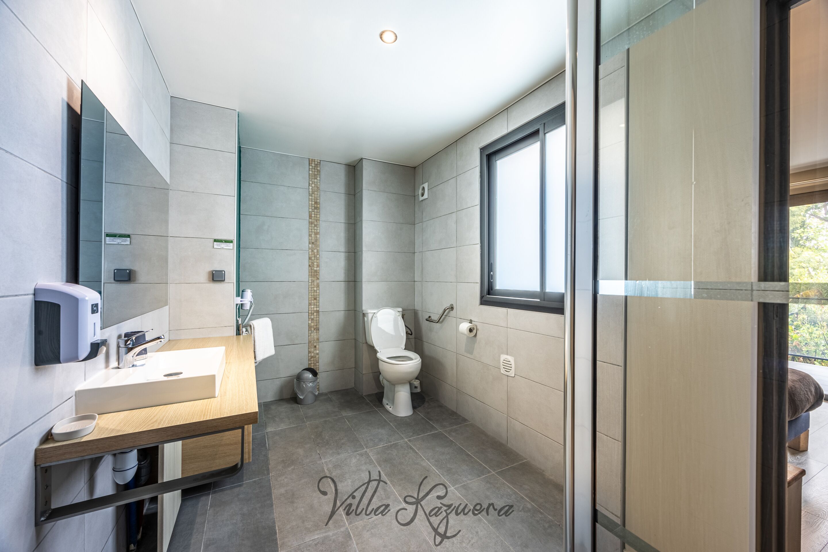 Une salle de bain moderne avec un meuble-lavabo en bois, des toilettes et une grande fenêtre.
