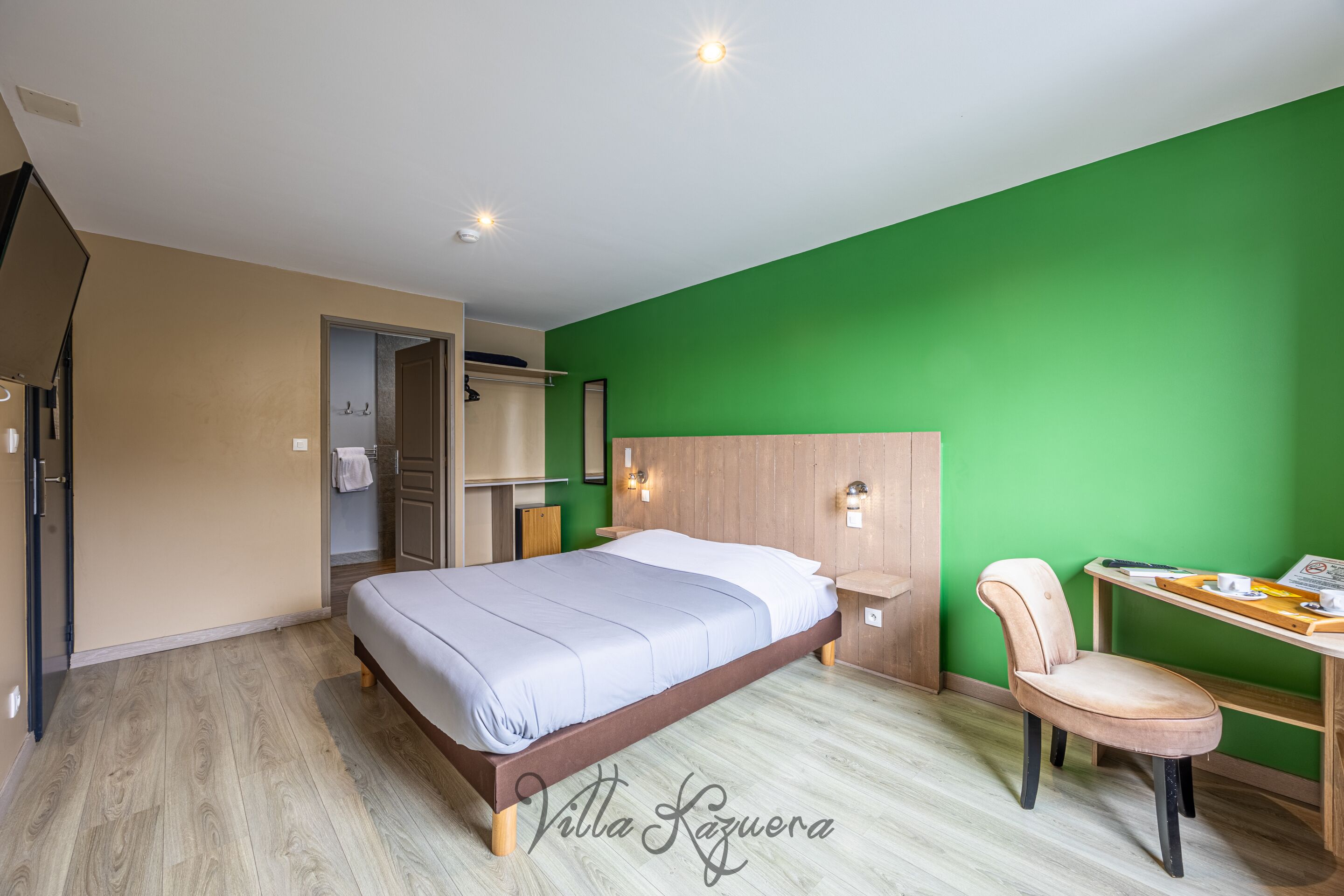 Camera d'albergo con un letto, una sedia, una scrivania e un muro verde.