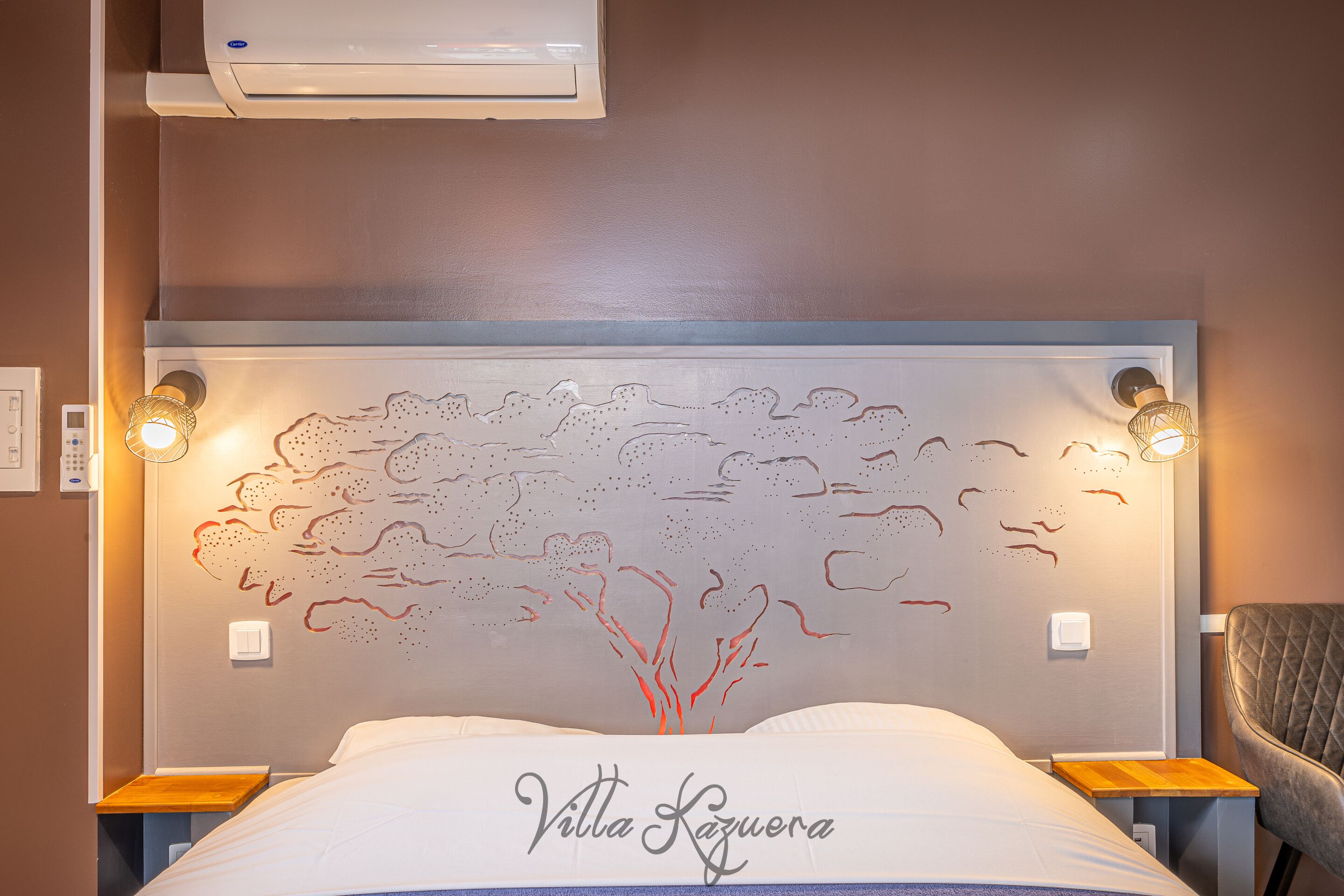A hotel room with a bed, a headboard with a tree design, two bedside lamps, and a chair.