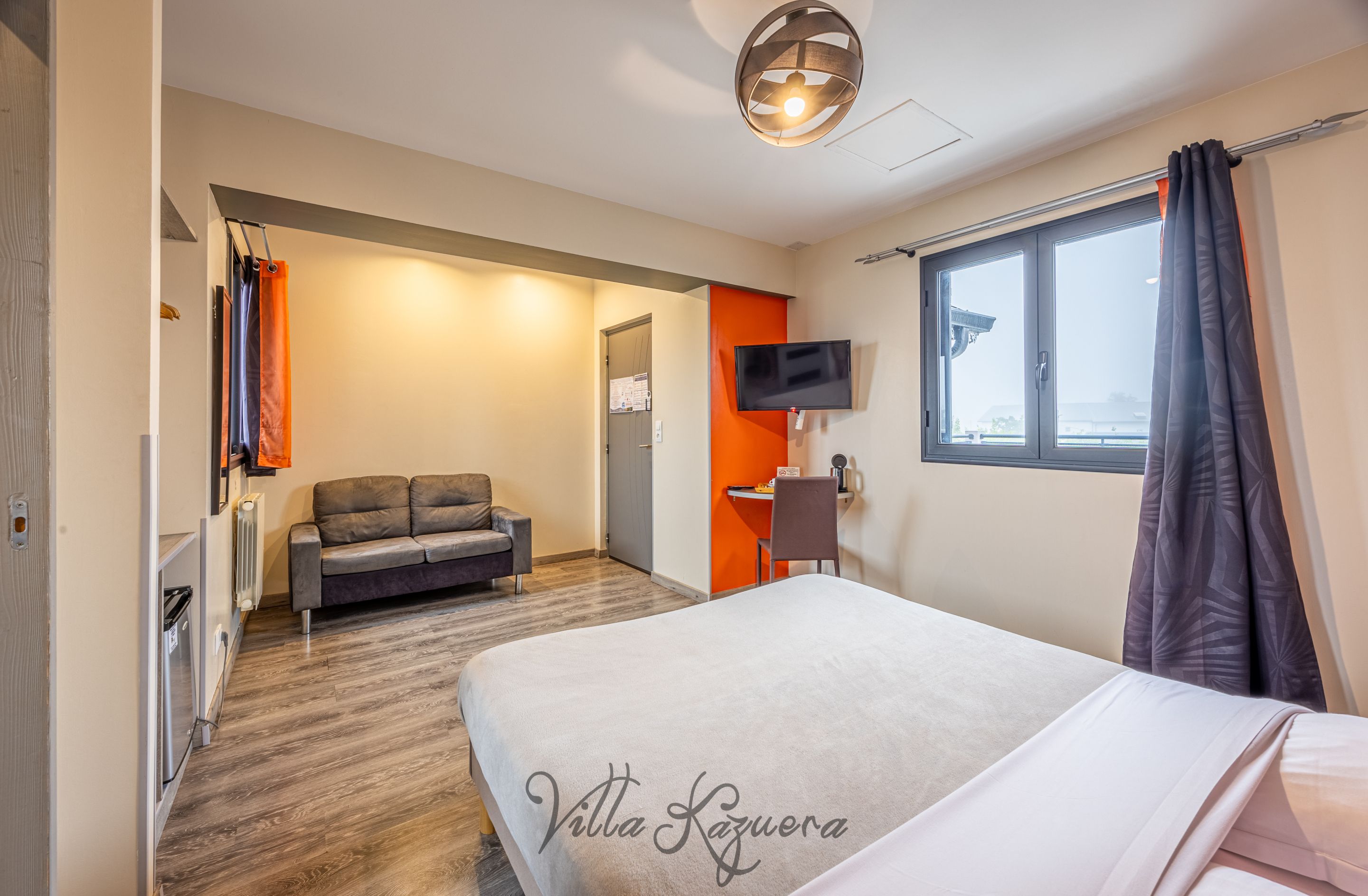 A hotel room with a bed, a sofa, a desk, a TV, and a window with curtains.