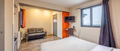 A hotel room with a bed, a sofa, a desk, a TV, and a window with curtains.