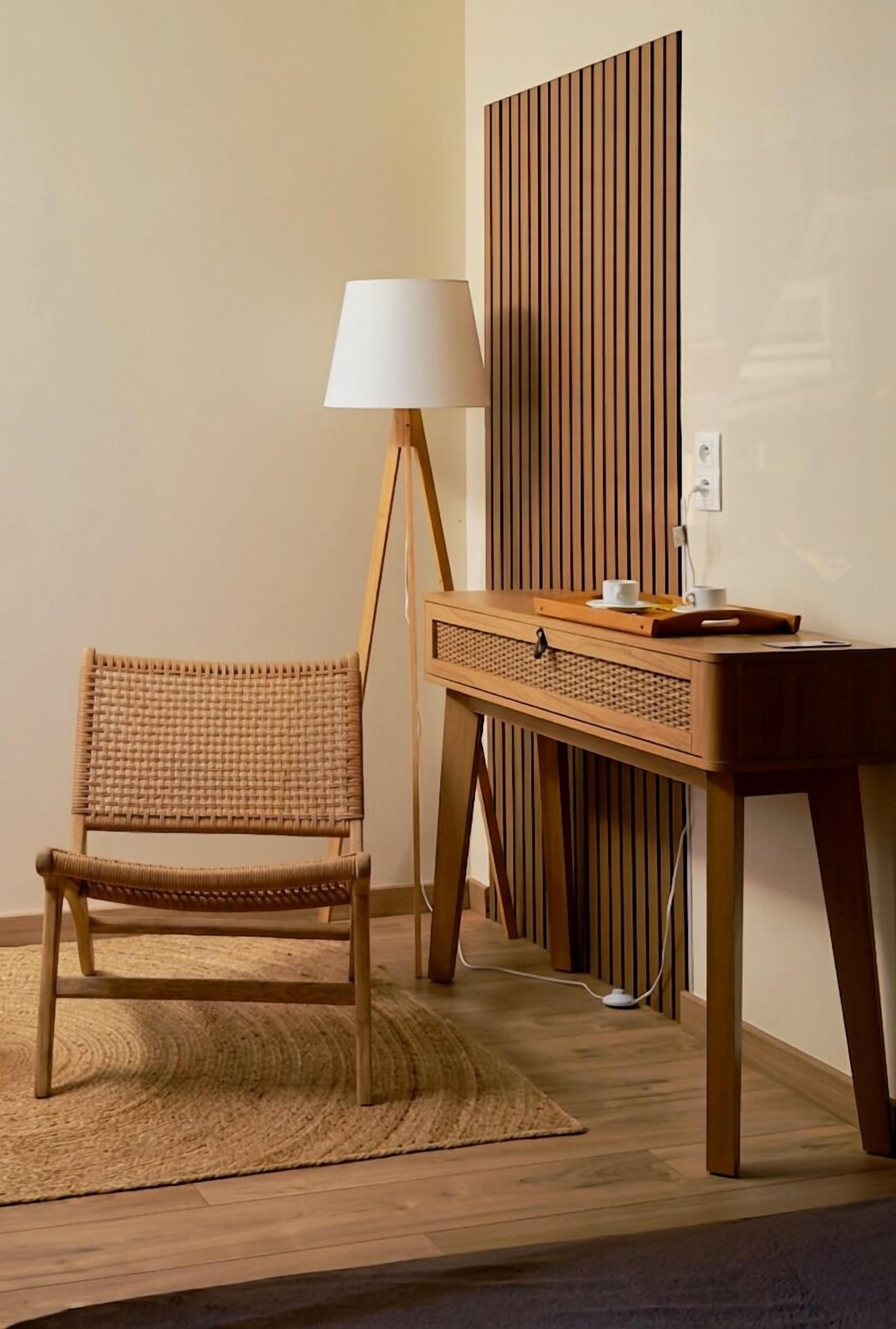 A room with a wicker chair, a wooden desk, a lamp, and a wall panel.