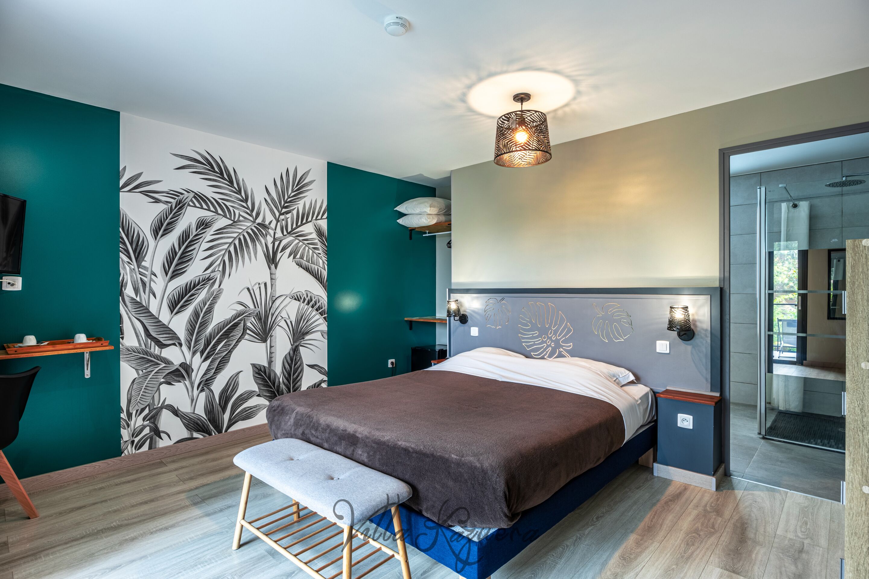 Une chambre à coucher moderne avec un lit, un banc, des œuvres d’art murales et un luminaire au plafond.