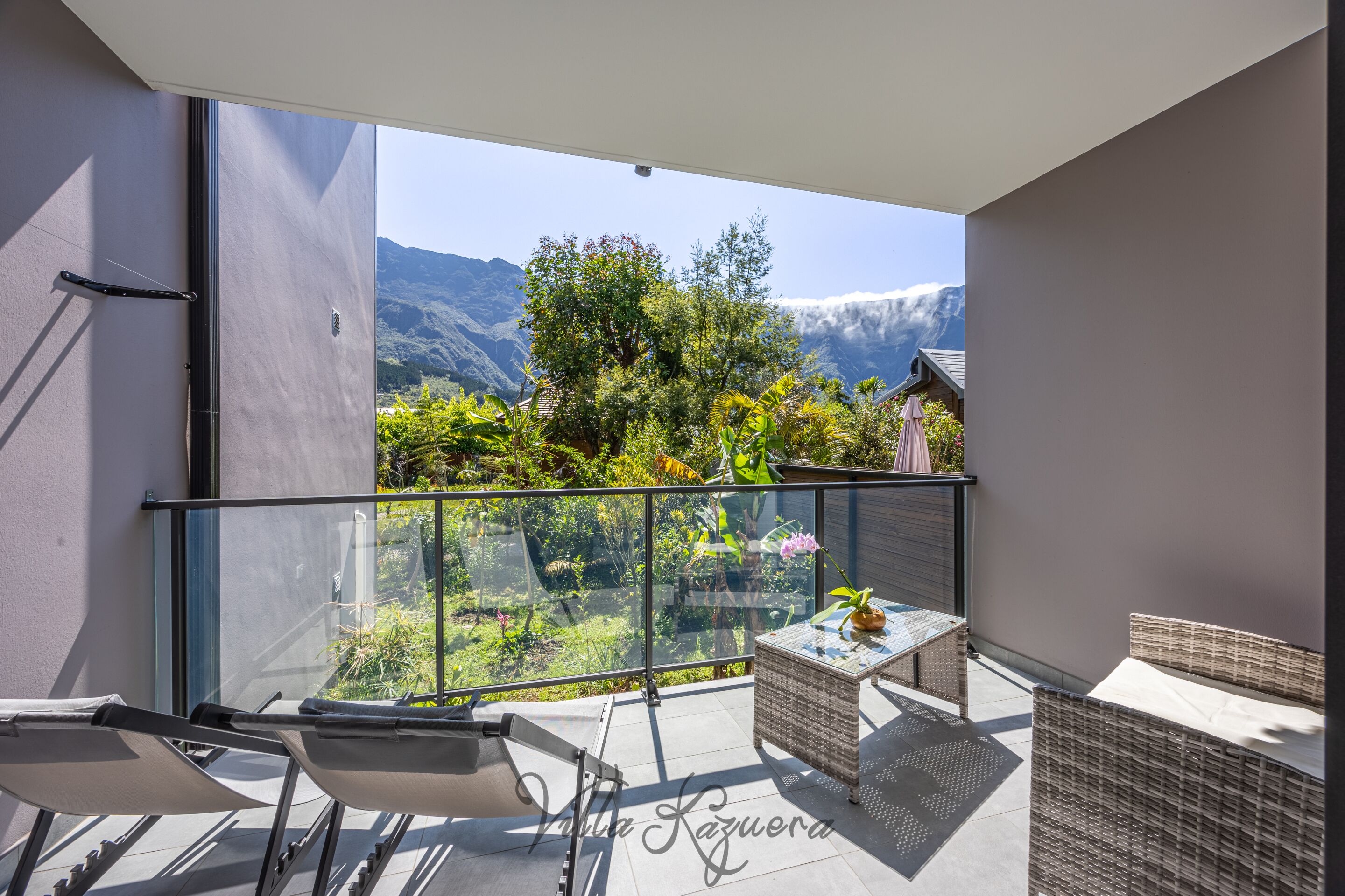 A balcony with a glass railing, wicker furniture, and a view of mountains.