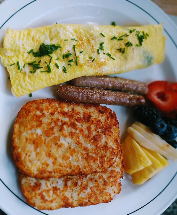 Un plato con una tortilla, salchichas, una hamburguesa a la plancha y fruta cortada.