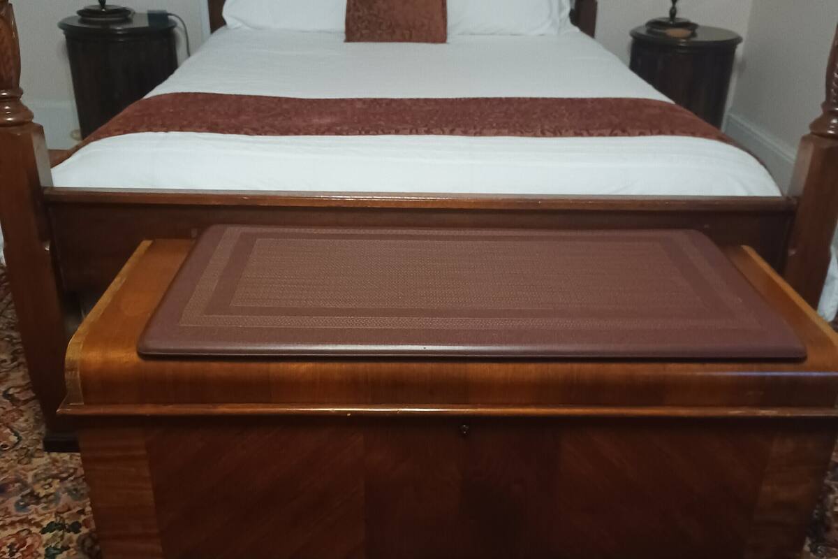 A neatly made bed with a brown headboard, a brown throw blanket, and two bedside tables with lamps.