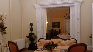 Relax in this stately room with a plush sofa set and armchairs, surrounded by elegant moldings and a high ceiling.